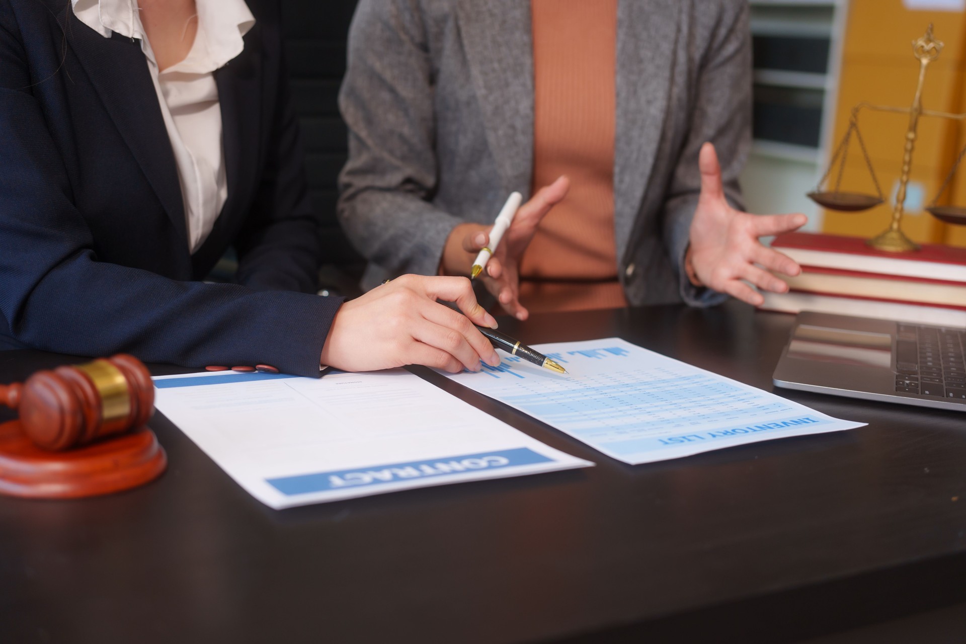 Primer plano de dos manos de abogadas trabajando en un escritorio, manejando documentos legales, redactando contratos y preparándose para reuniones de negocios, especializadas en servicios legales y legales corporativos